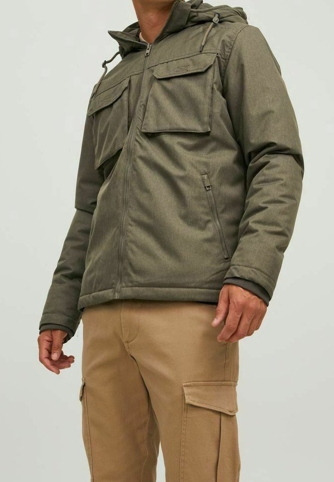 Homme portant une veste zippée vert olive avec deux poches à rabat sur la poitrine et un pantalon cargo beige avec des poches latérales.