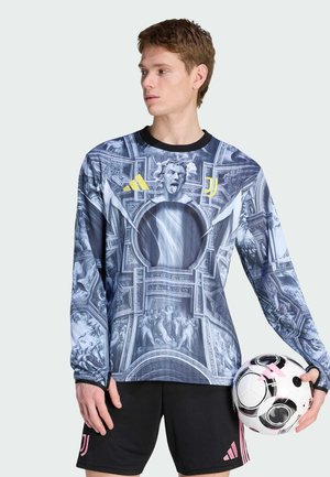 Langærmet, grafisk fodboldtrøje i blå med indviklede barokmønstre, med sort kant og gul logo, parret med sorte shorts og en fodbold.