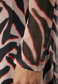 Tissu à manches longues à texture lisse présentant un motif de vagues en noir, rouge et crème. Détail de couture visible au niveau du poignet.
