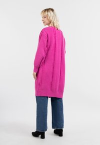 Jasnoróżowy długi kardigan z teksturowanymi pionowymi paskami, ściągaczami na mankietach i u dołu. Nosić go na niebieskich szerokich dżinsach i czarnych botkach.