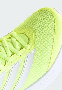 Pointe de chaussure de sport jaune vif avec des rayures blanches, tige en mesh texturé et lacets assortis sur une semelle blanche rembourrée.