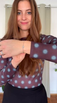 Pulsera de plata en una muñeca, con un pequeño adorno decorativo. Parte superior de color marrón oscuro con grandes lunares azul claro. Textura de tela suave.