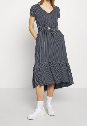 Robe rayée bleu marine avec des manches courtes, un col en V, des détails en boutons, une ceinture à la taille et un ourlet volanté. Associée à des baskets blanches et des chaussettes de chevilles.