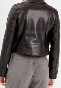 Sort læderjakke med figursyet design, let glans og kort længde. Bagsiden har syede detaljer og en glat tekstur. Kombineret med grå bukser.