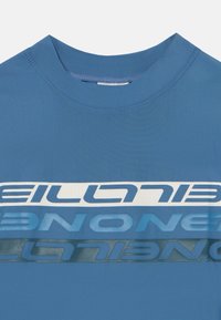 Blå kortärmad t-shirt med rund halsringning, med överlappande textgrafik i olika nyanser av blått och vitt. Slät textur.