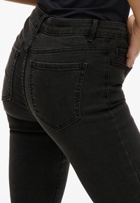 Vaqueros negros ajustados de denim, con una cintura alta, bolsillos traseros clásicos y una textura suave con costuras visibles mínimas.