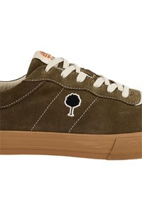 Sneaker in suede verde oliva con lacci bianchi, suola in gomma e logo nero dell'albero sul lato. I punti di colore contrastante esaltano il design.