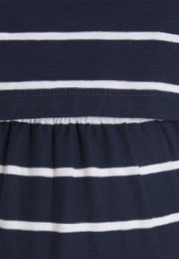 Granatowy materiał z białymi poziomymi paskami i detalami zebranych szwów, tworzącymi falowany wzór.