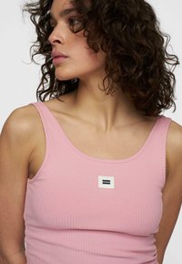 Roze geribbelde tanktop met brede banden, voorzien van een rechthoekig label met een zwart-wit grafisch ontwerp. Zachte textuur, aansluitende pasvorm.