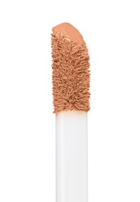 Concealerapplicator met een witte handgreep en een getextureerde, taps toelopende borstelpunt. De punt is bedekt met een perzikkleurig romig product.