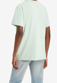 T-shirt vert menthe à manches courtes avec un col rond, fabriqué en coton. Il présente une coupe droite et une petite étiquette de marque sur la couture latérale.