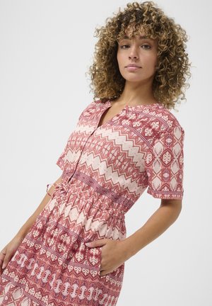 Short-sleeved dress with a V-neck, featuring a pink and cream geometric pattern, elastic waist, and side pockets. Lightweight fabric, flowy design.