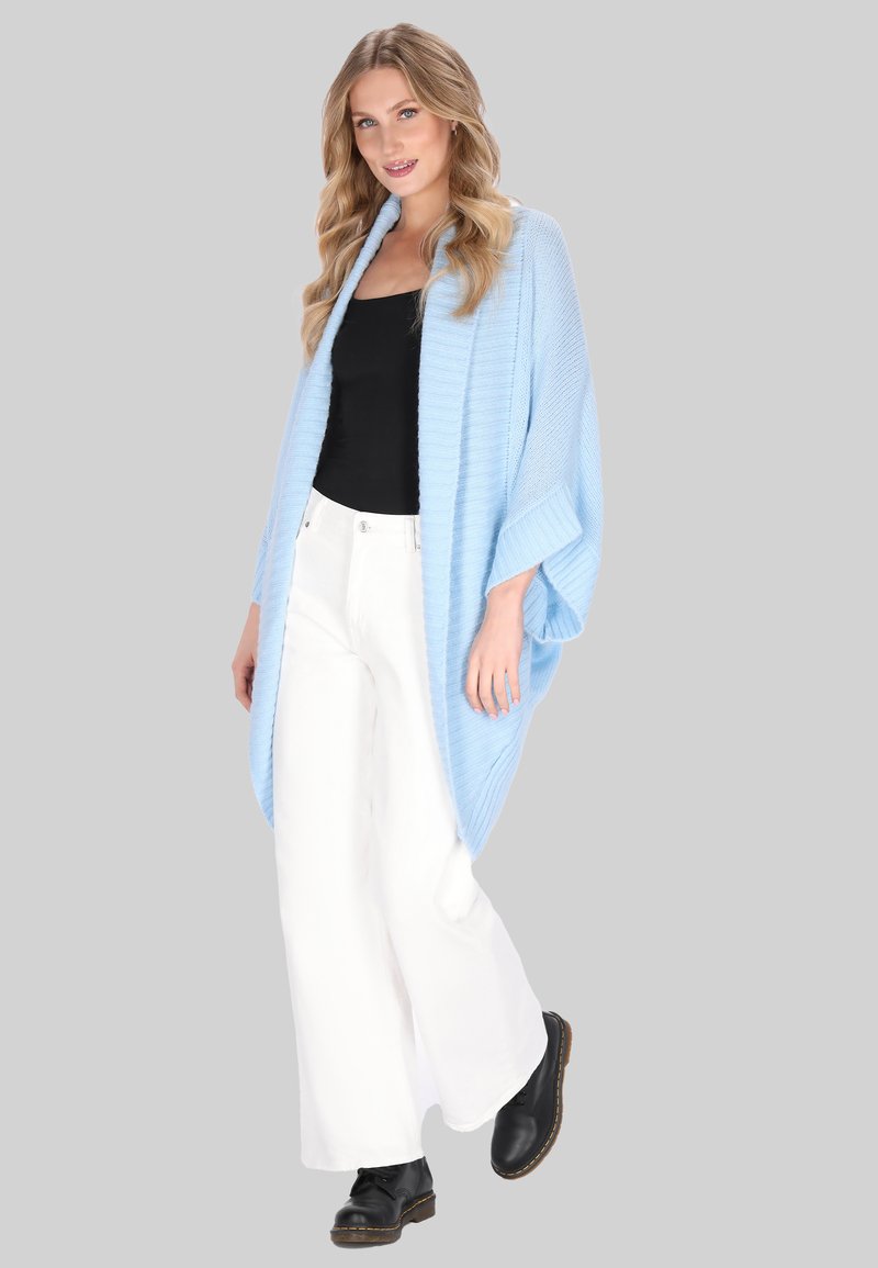 Lichtblauwe gebreide cardigan in kimono-stijl met een losse pasvorm, wijde mouwen en een geribbelde textuur, gecombineerd met een zwart topje en witte, wijde broekspijpen.