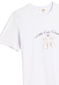 Camiseta blanca de algodón con un estampado en el frente de dos conejos enfrentados con un corazón, y el texto "Cosas Lindas" arriba.