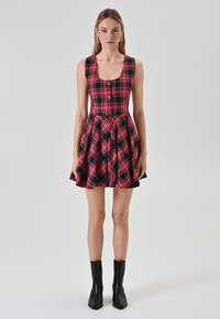 Abito a scacchi rosso e nero con corpino attillato, scollatura quadrata e gonna ampia con pieghe. Vengono indicate stivali neri alla caviglia.