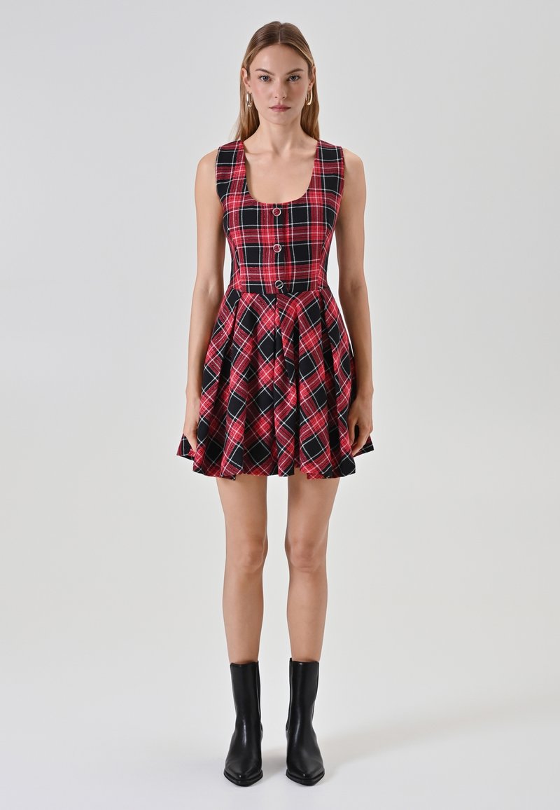 Abito a scacchi rosso e nero con corpino attillato, scollatura quadrata e gonna ampia con pieghe. Vengono indicate stivali neri alla caviglia.