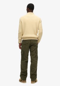 Beige geribbelde trui met een hoge hals, gecombineerd met losse olijfgroene cargobroeken met zijzakken en subtiele branding.