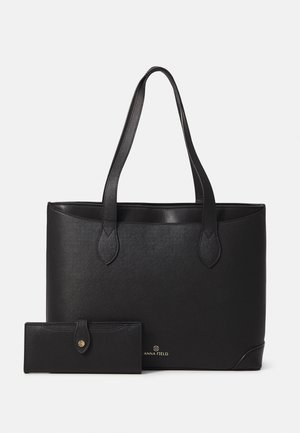 Sac tote noir avec surface texturée, poignées doubles et un portefeuille assorti. Présente un détail de logo subtil sur la partie inférieure du sac.