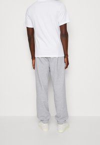 Camiseta de algodón blanca y pantalones de chándal grises, con una cinturilla elástica y puños, combinados con zapatillas de color claro.