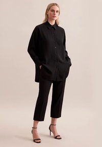 Camicia nera con bottoni, vestibilità comoda, maniche lunghe e tasche frontali, abbinata a pantaloni neri su misura cropped e tacchi neri con cinturini.