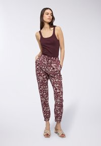 Top in bordeaux abbinato a pantaloni jogger a fantasia con un design floreale color crema. Scarpe: décolleté beige con dettagli intrecciati.