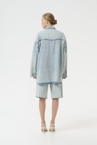 Giacca in denim oversize di un azzurro chiaro con orlo frangiato, abbinata a pantaloni shorts in denim coordinati. Tessuto morbido, spalle scese e vestibilità casual.