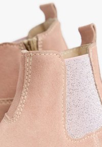 Stivali alla caviglia in camoscio rosa con un accento in argento texturizzato sul lato, con cuciture visibili e linguette per una facile calzata.