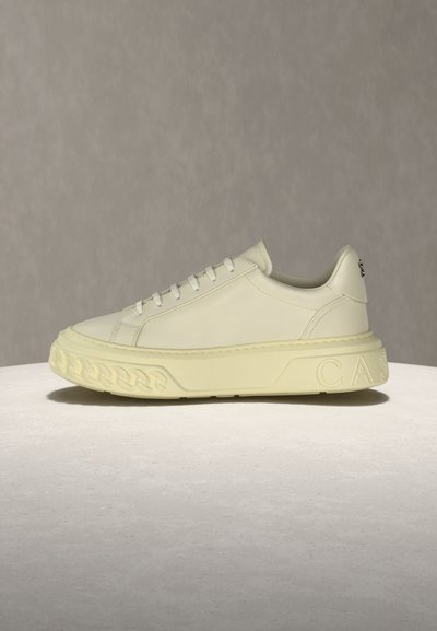 Εκρού χαμηλό sneaker με παχύ υφασμάτινο πάτο, στρογγυλεμένη μύτη, δέσιμο με κορδόνια και ανάγλυφες λεπτομέρειες στη φτέρνα και στην πλευρά.