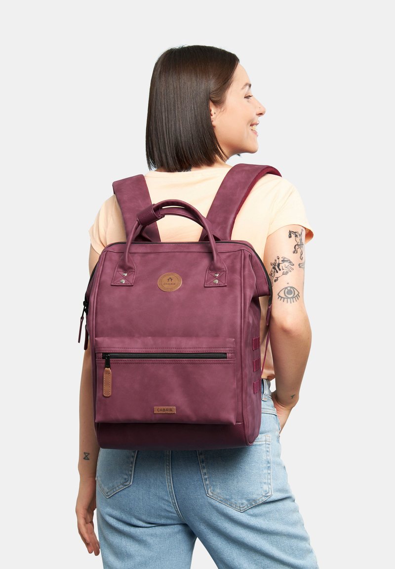 Zaino bordeaux con accessori metallici, tasche con zip e manici doppi. Realizzato in materiale sintetico texturizzato, con spallacci regolabili.