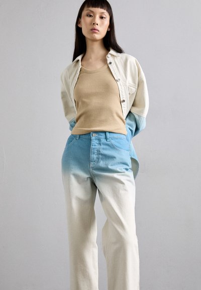Cămașă din denim bej cu mânecă lungă peste un top din bumbac bej cu nervuri, asortată cu blugi cu picioare largi în degrade de la albastru la alb. Texturi fine și croi lejer.