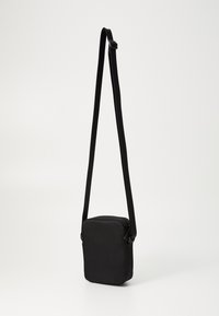 Malá čierna obdĺžniková crossbody taška s nastaviteľným popruhom, zipsovým uzáverom a jednoduchým minimalistickým dizajnom na bielom pozadí.