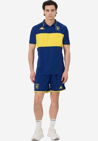 Maglietta polo sportiva blu e gialla con pantaloni abbinati, caratterizzata da un design a righe orizzontali, accenti con logo e rifiniture a contrasto.