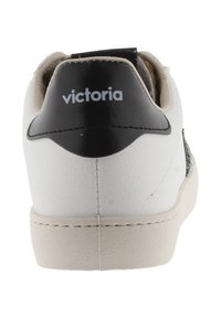 Baskets blanches avec une surface lisse, accent en cuir noir au talon et détails brodés. Présente le nom de la marque "Victoria" sur le talon.