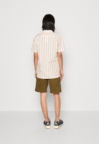 Lyhythihainen, raidallinen paita pehmeässä kerma- ja ruskeansävyssä; oliivinvihreät cargo-shortsit, joissa on taskuja; rentotennarit monivärisellä kuosilla.