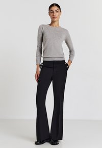 Maglione grigio a maniche lunghe con orlo a costine abbinato a pantaloni neri a vita alta con dettagli in bottone argentato e tasche laterali. Tessuto dalla texture liscia.