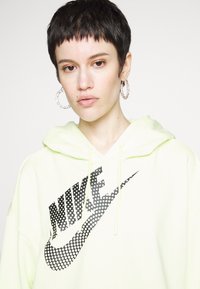 Felpa verde chiaro in morbido tessuto con un grande logo Nike nero in motivo a pois; include un cappuccio con cordino e polsini.