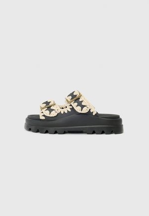 Sort platformsandal med tyk, ribbet sål og to stropper dekoreret med beige vævet broderi og justerbare spænder.