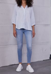 Jasnoniebieska koszula na guziki w paski z dekoltem w serek, zestawiona z jasnoniebieskimi obcisłymi dżinsami i białymi tenisówkami. Gładka tkanina i casualowy krój.