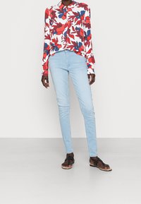 Floral long-sleeve shirt in white with red and blue patterns, paired with light blue skinny jeans and black flat sandals.