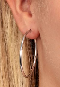 Orecchino a cerchio d'argento esposto su un orecchio forato. L'orecchino presenta una superficie liscia e lucida con un design circolare e sottile.
