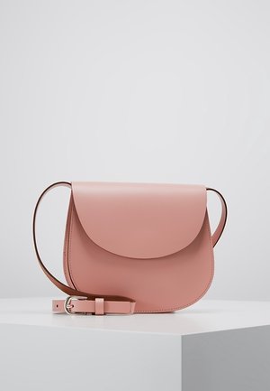 Lyserød læder crossbody taske med buet klap og justerbar rem placeret på en hvid overflade mod en lys grå baggrund.