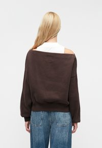 Sudadera marrón de gran tamaño con un diseño ancho de hombros caídos, tejido texturizado y puños acanalados, combinada con pantalones vaqueros de tiro alto en azul claro.