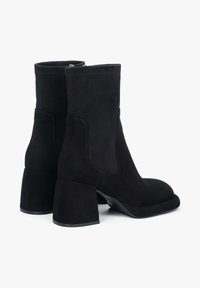 Zwarte suède enkelboots met een ronde neus, blokhak, elastische zijpanelen en een zichtbare rits aan de achterkant.