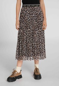 Peurta midi skirta su leopardų raštu, su juodu elastingu juosmeniu, ant kurio kartojasi žodis "MEILĖ", dėvima su smėlio spalvos kojinėmis ir rudomis masyviomis batų raištelių avalyne.