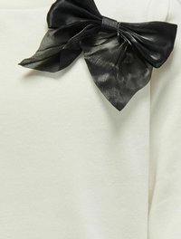 Lichtbeige top met een textuur van zwarte satijnen strikaccent, van zachte stof en met een ronde hals. De strik is gedetailleerd met gelaagde stof.