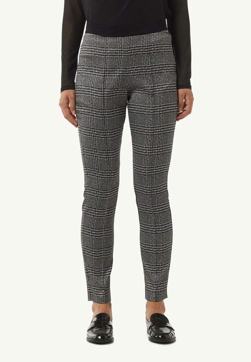 Czarno-białe spodnie w kratę o dopasowanym kroju, gładkiej strukturze, płaskim przodzie i zwężanych nogawkach, w połączeniu z błyszczącymi czarnymi mokasynami.