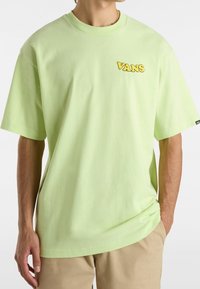 Camiseta de algodón verde claro con mangas cortas, con un logo amarillo de "VANS" en el pecho y un ajuste relajado.