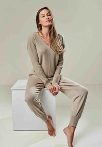 Beiges gestricktes Loungewear-Set mit einem V-Ausschnitt-Top und gerippten Akzenten sowie Jogginghosen mit Bündchen. Weicher Stoff und lockere Passform.