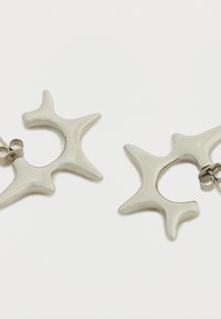 Ασημένια σκουλαρίκια με σχέδιο που μοιάζει με αστέρι. Λείο επιφάνεια, αφηρημένο σχήμα με αιχμηρές άκρες, διαθέτουν ασφαλές κούμπωμα για στερέωση.