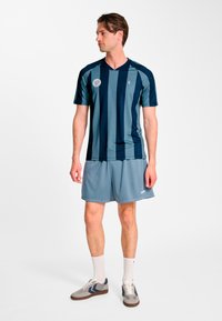 Granatowo-turkusowa sportowa koszulka w paski z dekoltem w serek, w połączeniu z jasnoszarymi siateczkowymi szortami i szarymi trampkami z granatowymi akcentami.